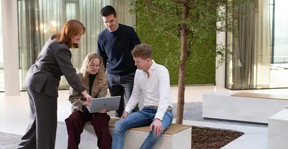 Group of people gathered in a green space area looking at a laptop